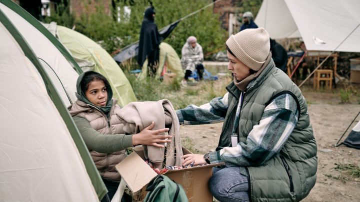 young-female-volunteer-passing-clothes-to-child-2021-10-20-03-13-59-utc
